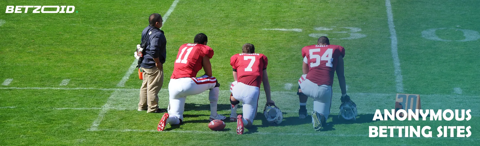 Three American football players stand on one knee on the field.