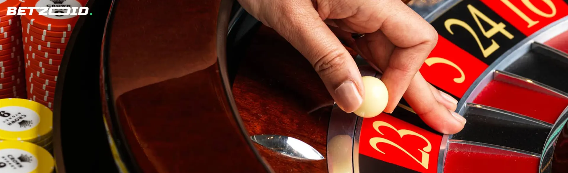 La mano de un jugador sostiene una bola sobre una rueda de ruleta de casino.