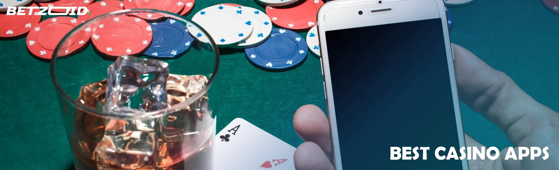A glass with a drink, cards, chips and a smartphone on a poker table.