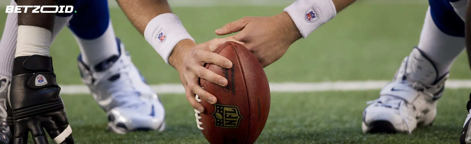 American football player's hands hold the ball on the grass.
