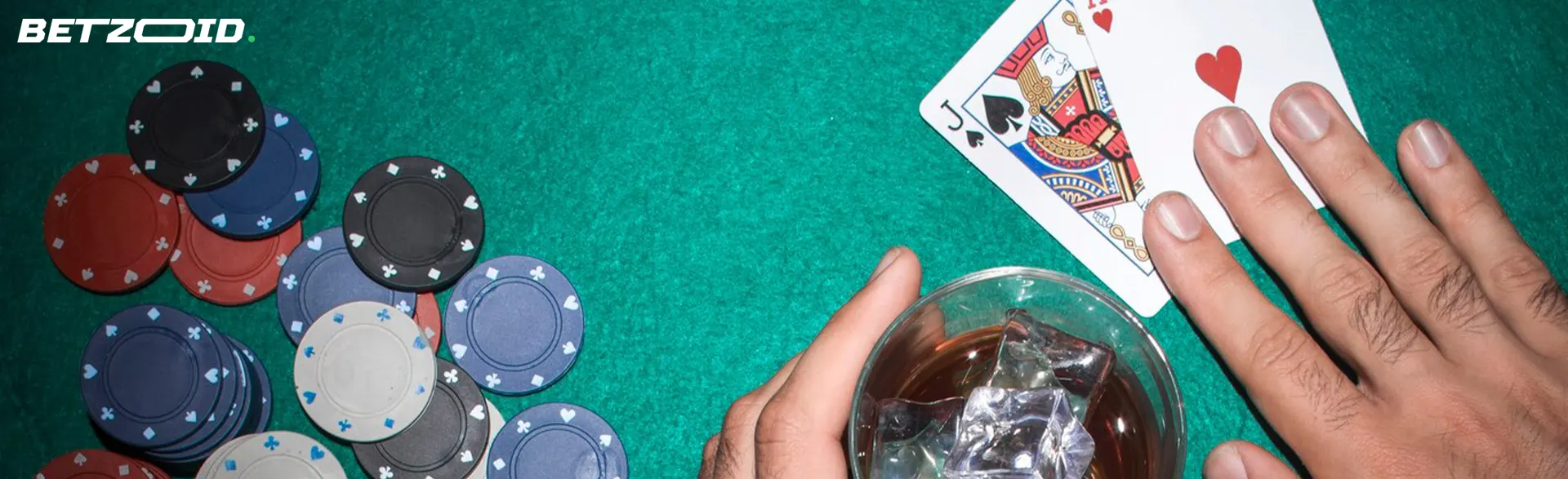 A player holds cards next to casino chips and a drink in a glass.