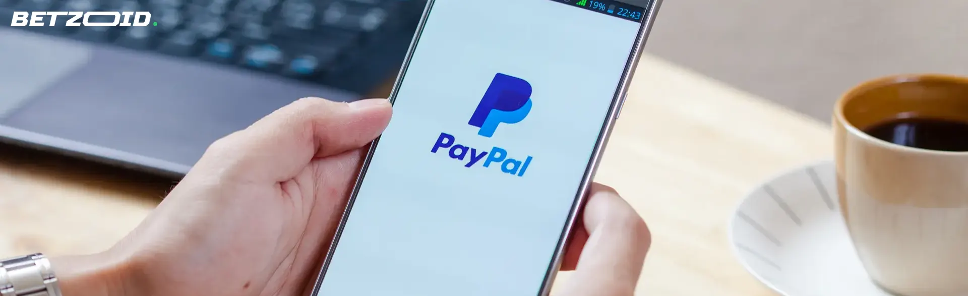 Eine Person hält ein Smartphone mit dem PayPal-Logo.