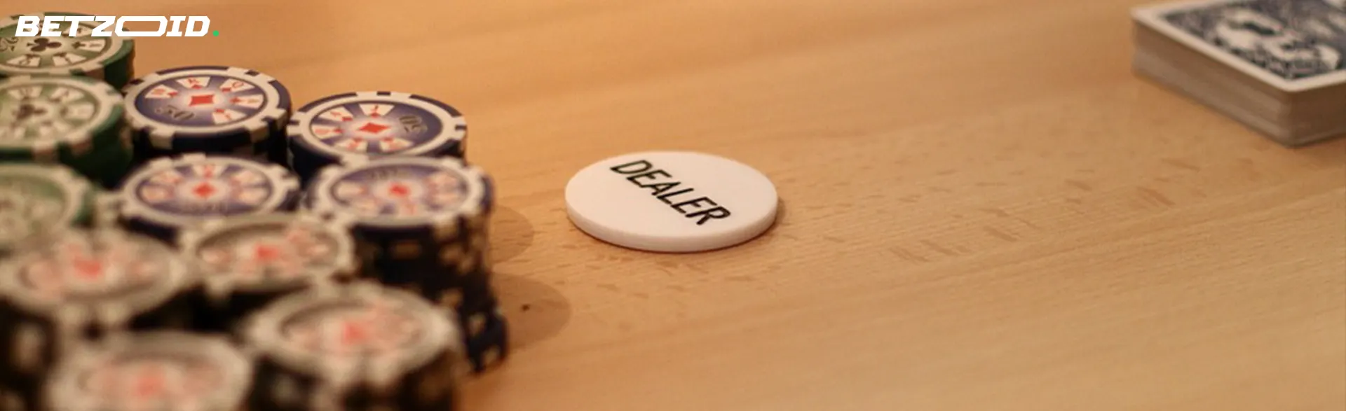 Poker chips stacked beside a 'DEALER' button and a deck of cards on a wooden table.