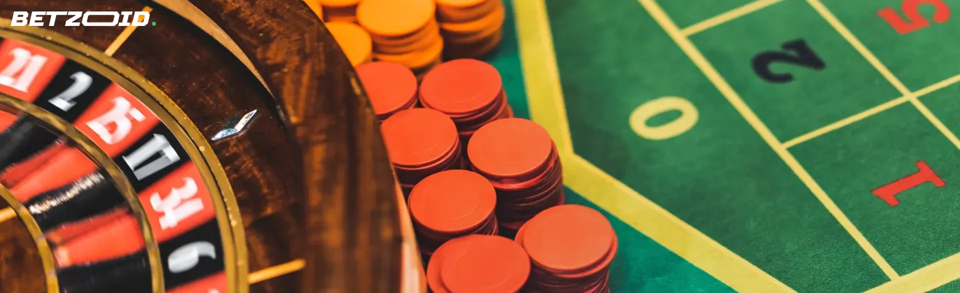 Close-up view of a roulette wheel next to stacks of red and orange chips on a green betting table.