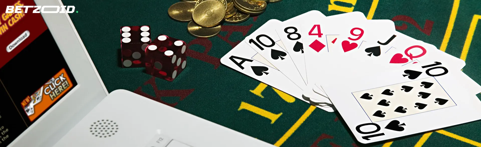 Carte da poker, dadi rossi e monete d'oro su un tappetino da gioco verde accanto a un laptop.