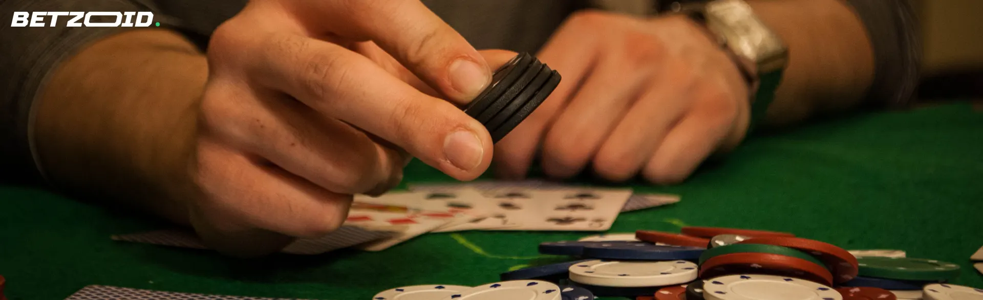 A player holds chips on a table with poker cards.