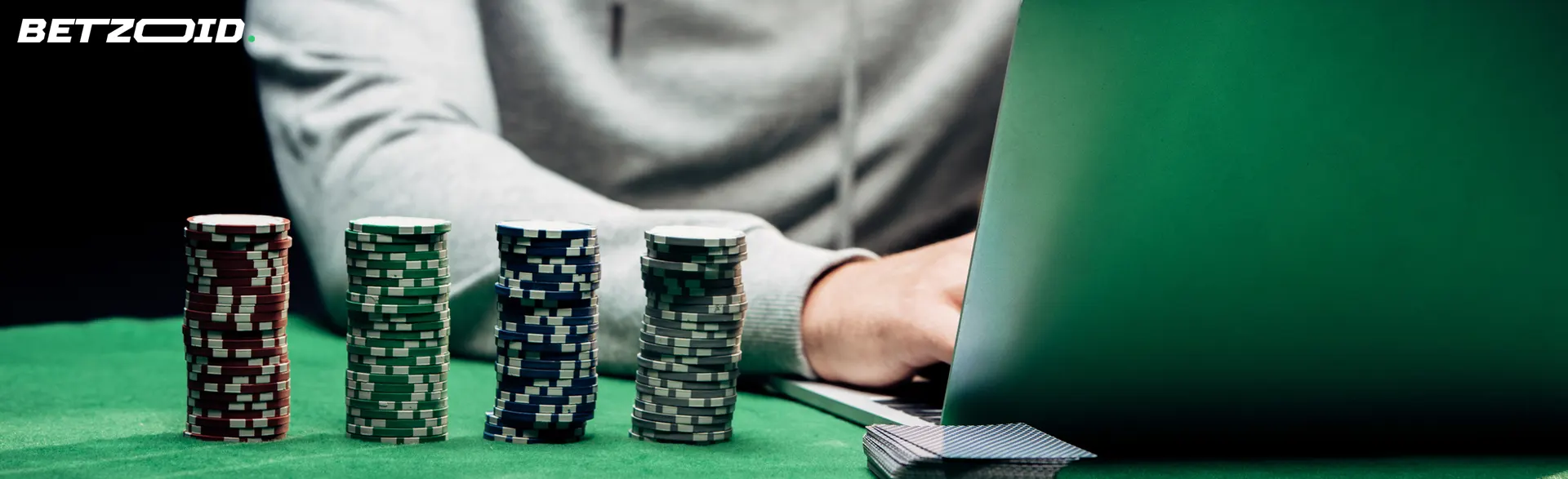 Hráč u notebooku vedle hromady kasinových žetonů.