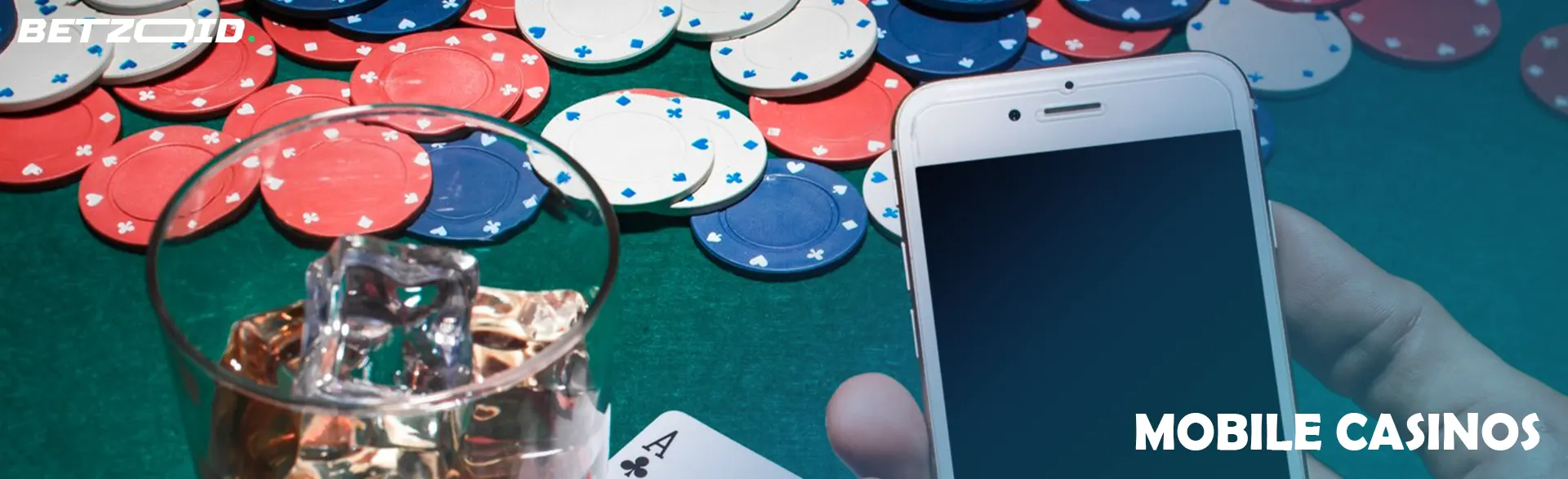 The player is holding a smartphone next to a drink in a glass on the background of casino chips.