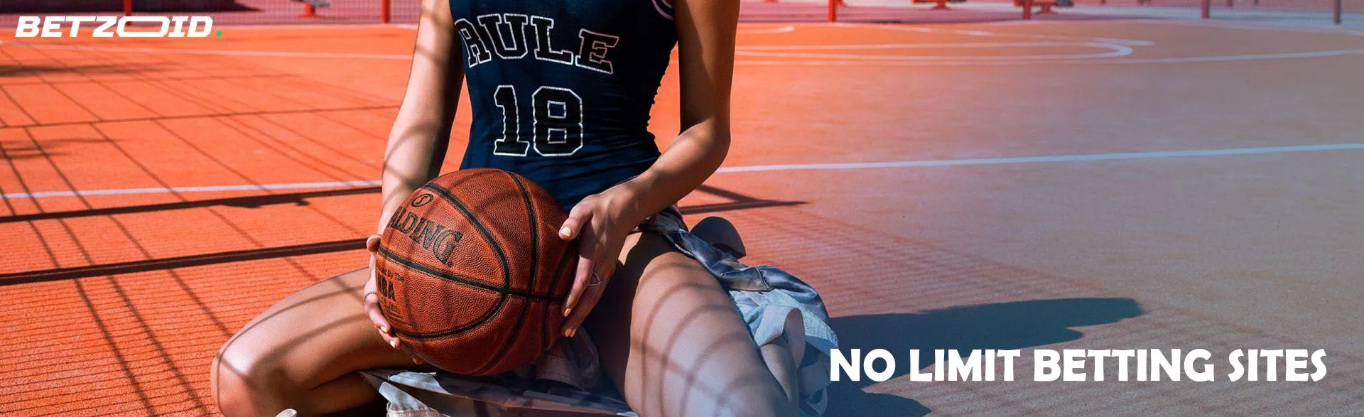 A woman basketball player sits with a ball on the court.