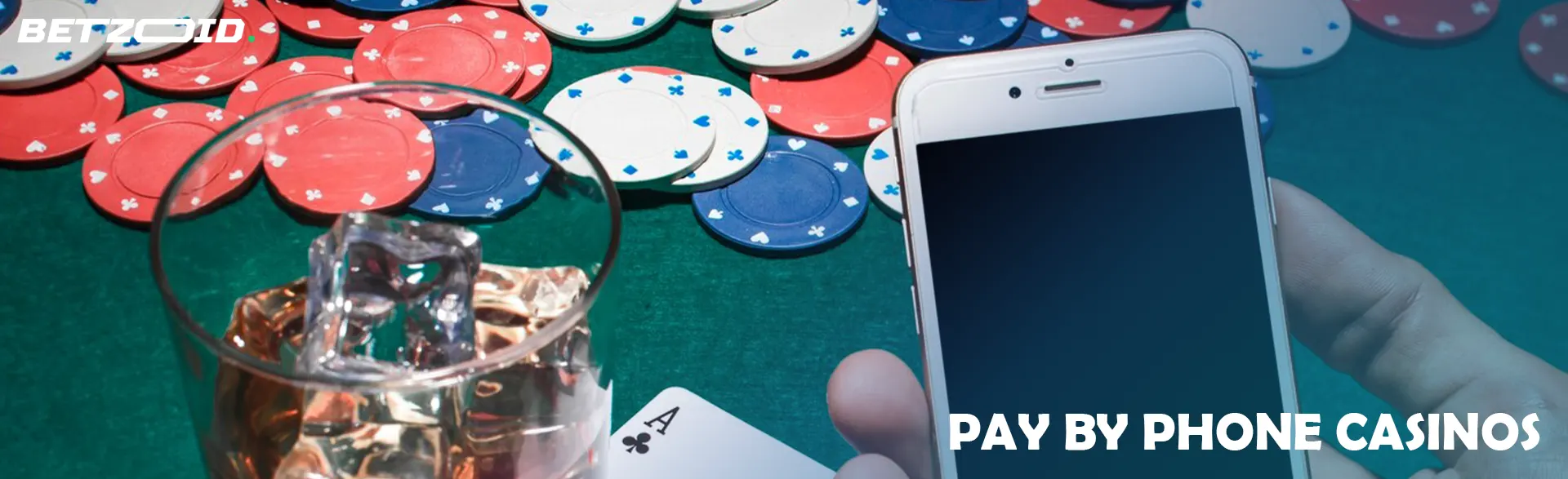 A player holds a smartphone next to casino chips and a drink in a glass.