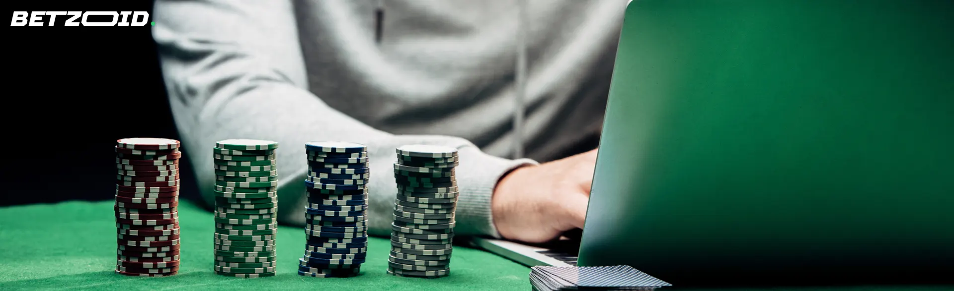 A player at a laptop next to stacks of casino chips.